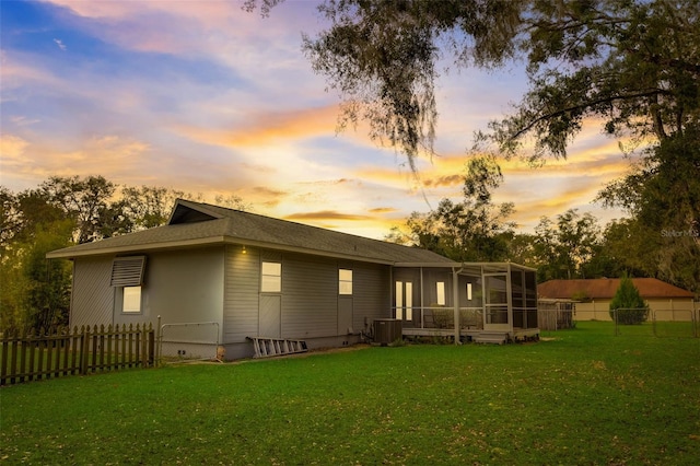 back house at dusk with central AC unit, a sunroom, and a yard