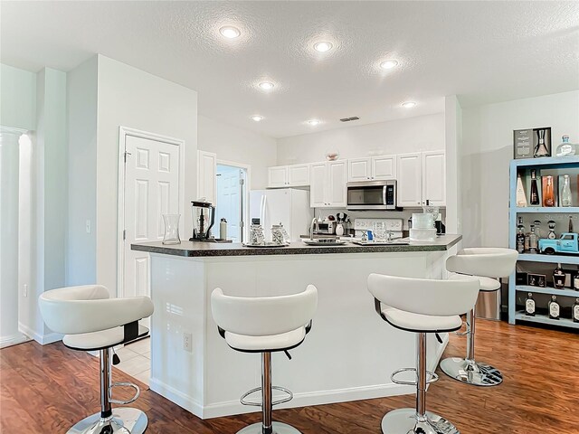 kitchen with hardwood / wood-style floors, white fridge with ice dispenser, a textured ceiling, and white cabinets