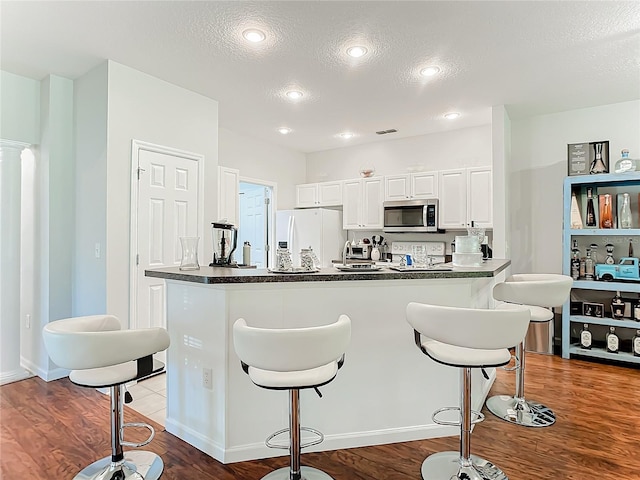 kitchen featuring white fridge with ice dispenser, dark countertops, stainless steel microwave, and a kitchen breakfast bar