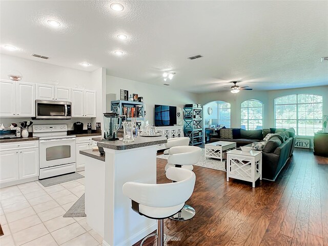 kitchen featuring light hardwood / wood-style floors, white cabinetry, electric range, ceiling fan, and a breakfast bar