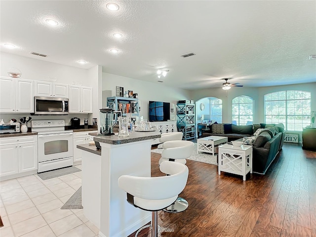 kitchen featuring electric range, stainless steel microwave, dark countertops, and visible vents