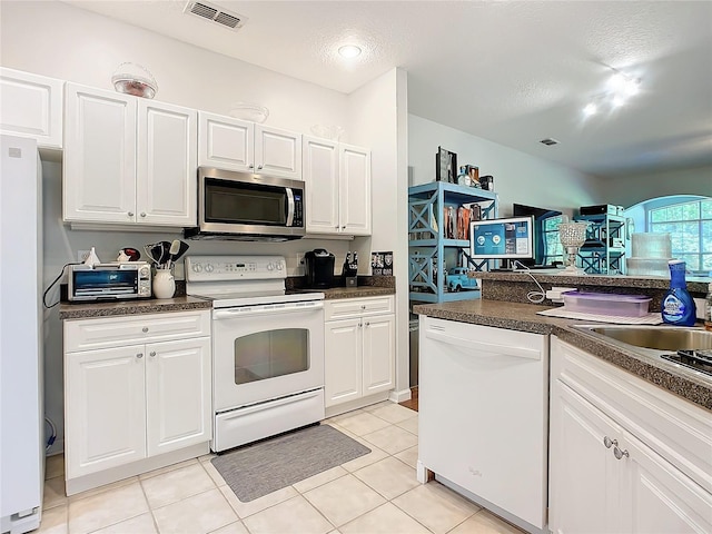 kitchen with dark countertops, white appliances, visible vents, and white cabinets