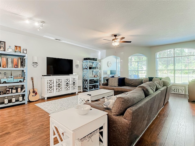 living area featuring arched walkways, ceiling fan, a textured ceiling, wood finished floors, and visible vents