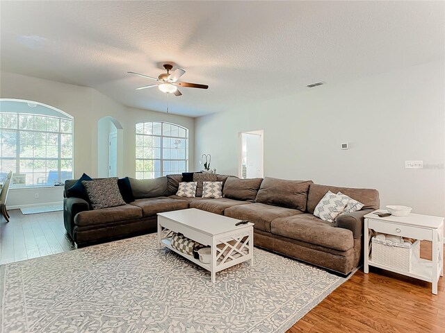 living room featuring light wood-type flooring, ceiling fan, and a textured ceiling