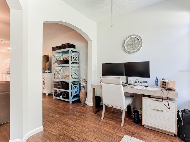 office area featuring baseboards, a textured ceiling, arched walkways, and wood finished floors