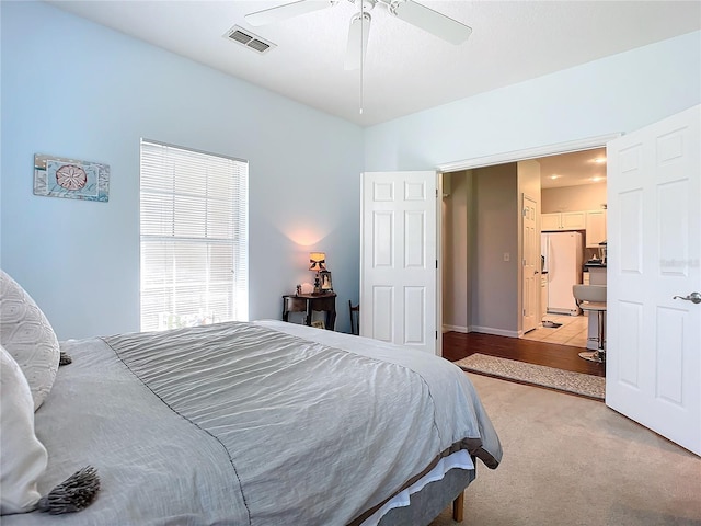 bedroom with ceiling fan, white refrigerator with ice dispenser, visible vents, and light colored carpet