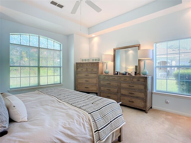 carpeted bedroom with ceiling fan and a raised ceiling