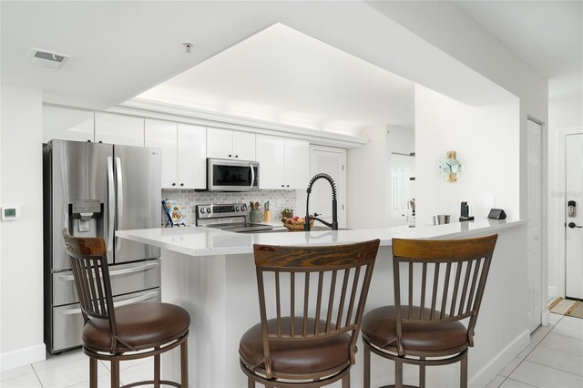 kitchen with visible vents, backsplash, a breakfast bar, white cabinets, and stainless steel appliances