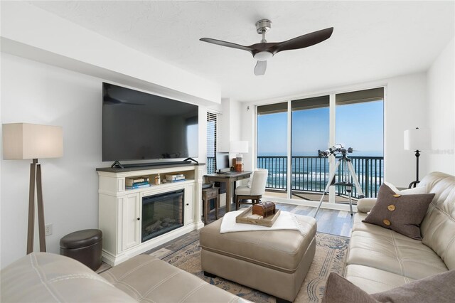 living room featuring a glass covered fireplace, a wall of windows, wood finished floors, and a ceiling fan