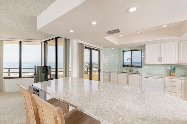 kitchen featuring light carpet, a raised ceiling, dishwasher, white cabinetry, and a sink