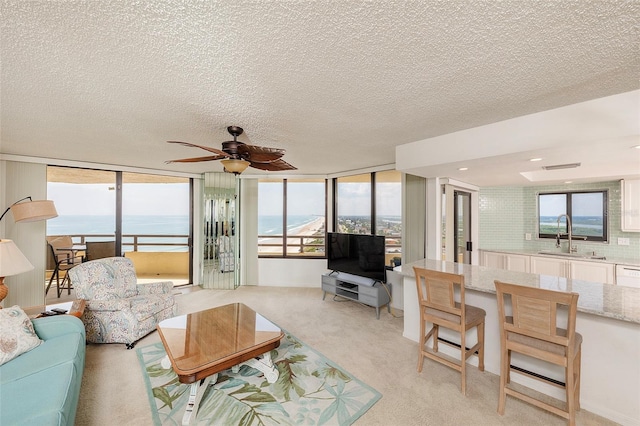 living area with a ceiling fan, light colored carpet, plenty of natural light, and a textured ceiling