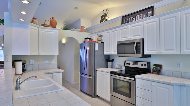 kitchen with appliances with stainless steel finishes, lofted ceiling, white cabinets, and sink