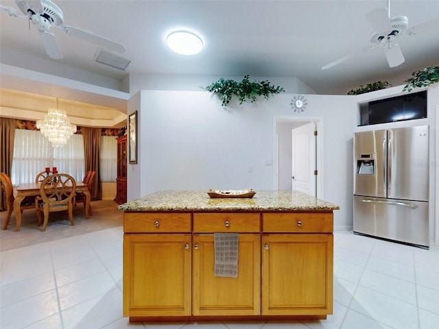 kitchen with stainless steel fridge, light tile patterned flooring, light stone countertops, and ceiling fan with notable chandelier