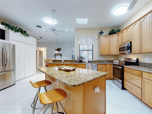 kitchen featuring a skylight, light stone countertops, a kitchen island, a kitchen bar, and stainless steel appliances