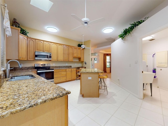 kitchen with a breakfast bar, a center island, sink, ceiling fan, and stainless steel appliances