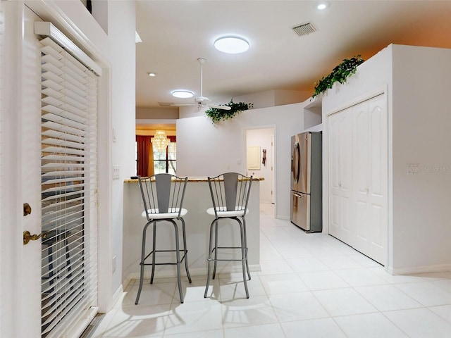 kitchen with a breakfast bar area, stainless steel refrigerator, and light tile patterned flooring