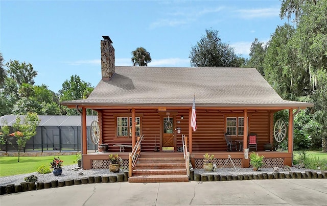 cabin featuring covered porch, a shingled roof, log exterior, a front lawn, and a chimney