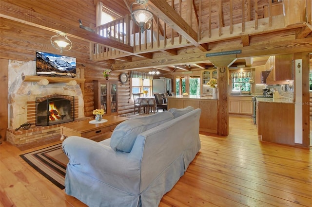 living area featuring a fireplace, a towering ceiling, light wood-style floors, log walls, and beamed ceiling