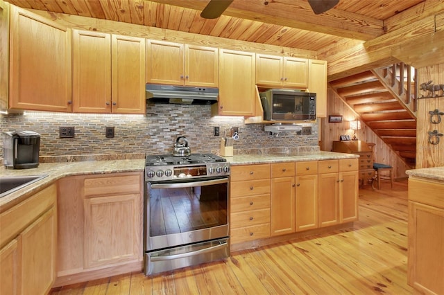 kitchen with under cabinet range hood, stainless steel gas range oven, tasteful backsplash, and light wood-style floors