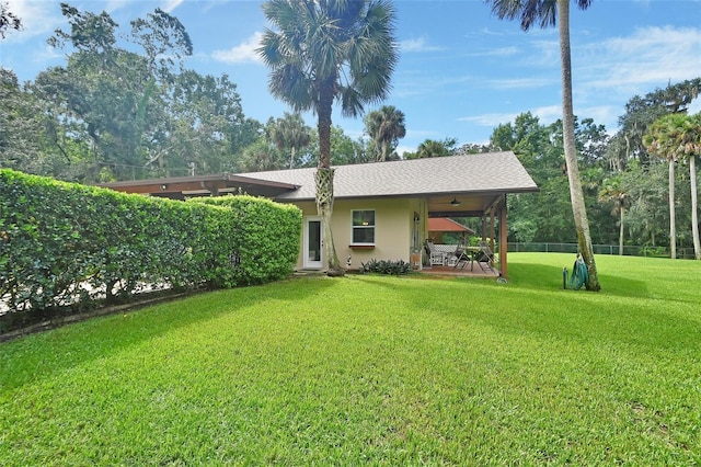 view of front facade with a front lawn, roof with shingles, fence, and stucco siding