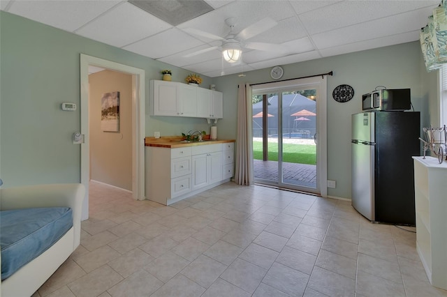 kitchen featuring a paneled ceiling, a ceiling fan, freestanding refrigerator, white cabinetry, and a sink