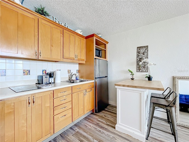 kitchen with a textured ceiling, light hardwood / wood-style floors, stainless steel refrigerator, sink, and decorative backsplash