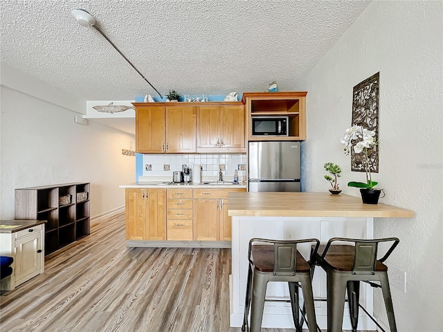 kitchen with a breakfast bar area, light hardwood / wood-style flooring, backsplash, stainless steel refrigerator, and black microwave