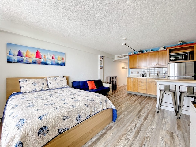 bedroom with a textured ceiling, stainless steel refrigerator, and light hardwood / wood-style flooring