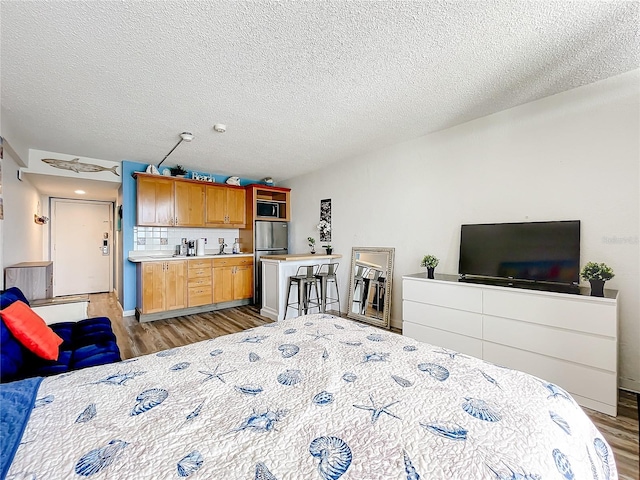 bedroom featuring a textured ceiling, stainless steel refrigerator, and light hardwood / wood-style floors