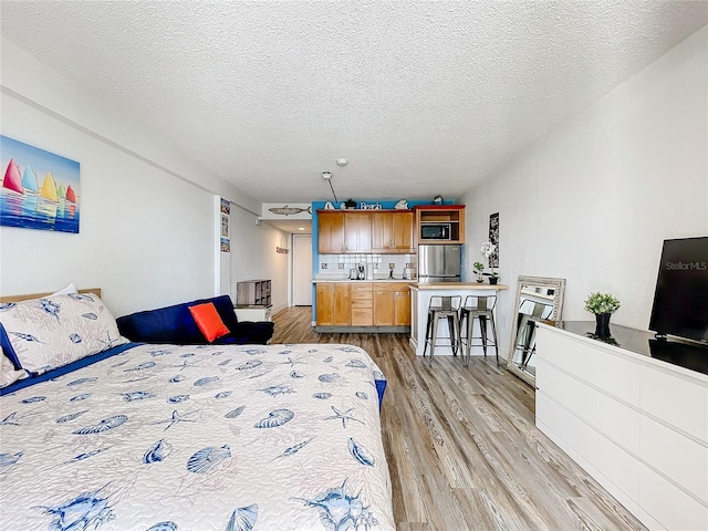 bedroom featuring a textured ceiling, stainless steel refrigerator, and light hardwood / wood-style floors