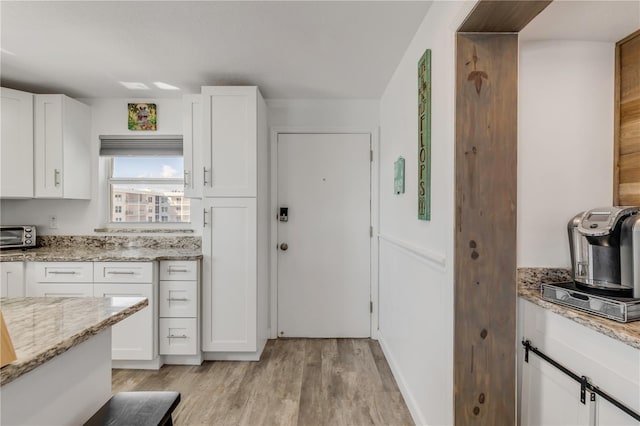 kitchen featuring a toaster, light wood-type flooring, white cabinetry, and light stone countertops