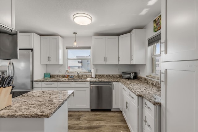 kitchen with light stone counters, stainless steel appliances, white cabinets, a sink, and wood finished floors