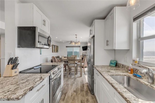 kitchen with stainless steel appliances, white cabinetry, a sink, and light wood-style flooring