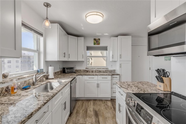 kitchen featuring a sink, white cabinets, appliances with stainless steel finishes, light wood finished floors, and decorative light fixtures