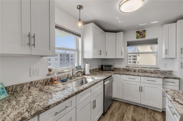 kitchen with wood finished floors, stainless steel dishwasher, a sink, and white cabinets