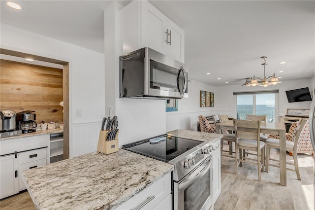 kitchen featuring light stone counters, white cabinetry, appliances with stainless steel finishes, wainscoting, and light wood-type flooring