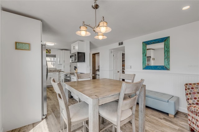 dining room featuring light wood finished floors, visible vents, and wainscoting