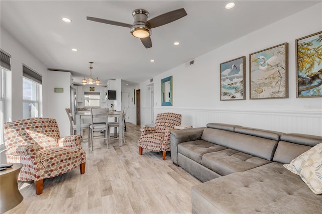 living area with recessed lighting, visible vents, light wood-style flooring, wainscoting, and ceiling fan with notable chandelier