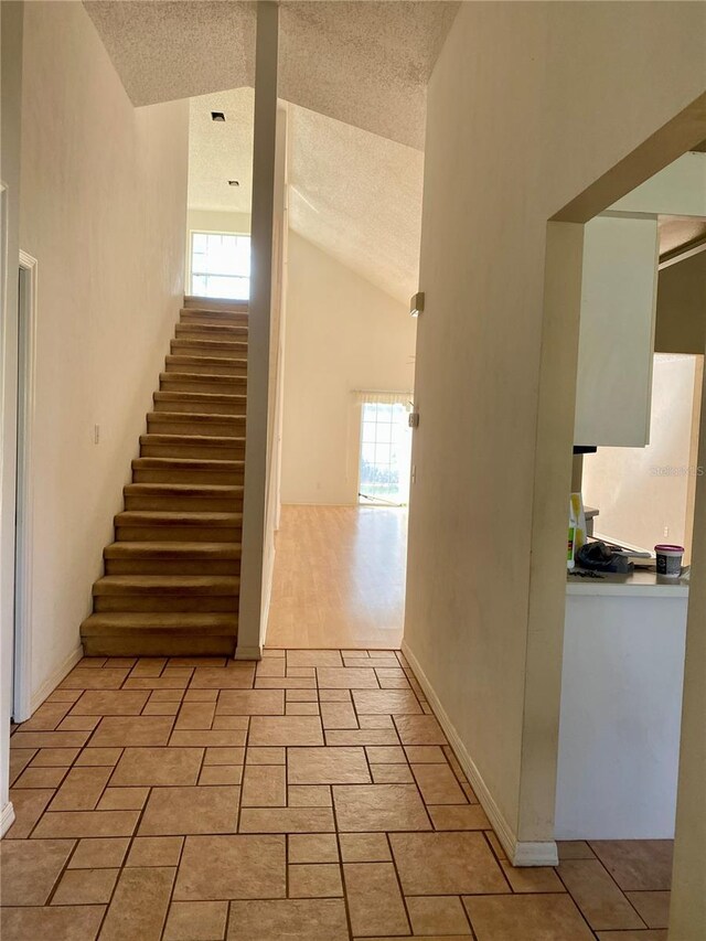 staircase with high vaulted ceiling, wood-type flooring, and a textured ceiling