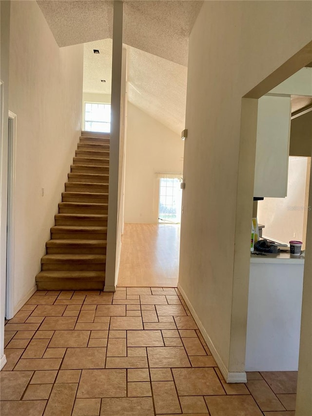 staircase featuring a healthy amount of sunlight, high vaulted ceiling, baseboards, and a textured ceiling