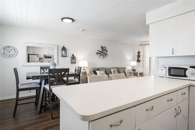 kitchen with a textured ceiling, white appliances, dark wood-type flooring, kitchen peninsula, and white cabinetry