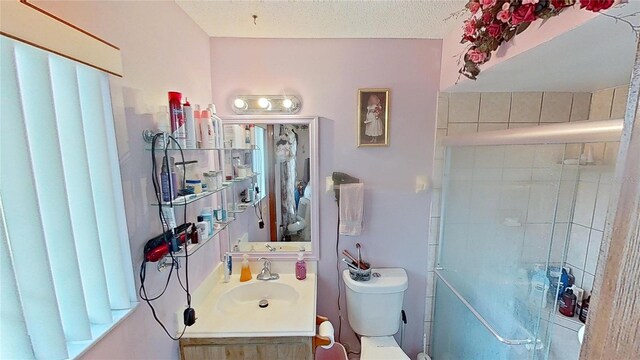 bathroom with a textured ceiling, vanity, toilet, and a shower with shower door