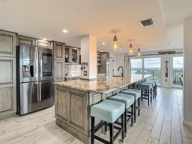 kitchen with a large island with sink, stainless steel fridge, light stone counters, a breakfast bar area, and light hardwood / wood-style floors