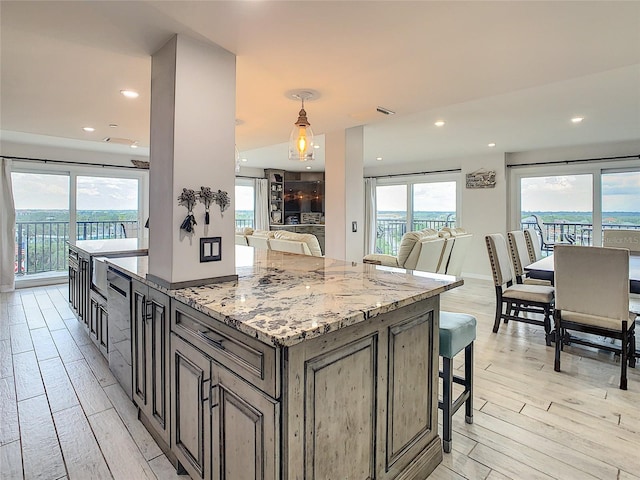 kitchen with a center island, light hardwood / wood-style flooring, light stone countertops, a breakfast bar area, and pendant lighting