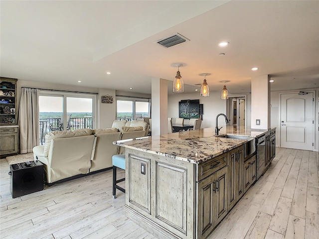 kitchen featuring decorative light fixtures, light hardwood / wood-style floors, light stone counters, and an island with sink