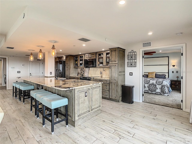 kitchen with light wood-type flooring, pendant lighting, tasteful backsplash, a breakfast bar, and a large island