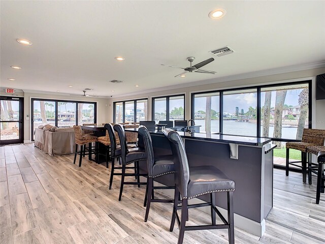 kitchen with light hardwood / wood-style flooring, a water view, ceiling fan, a kitchen bar, and ornamental molding