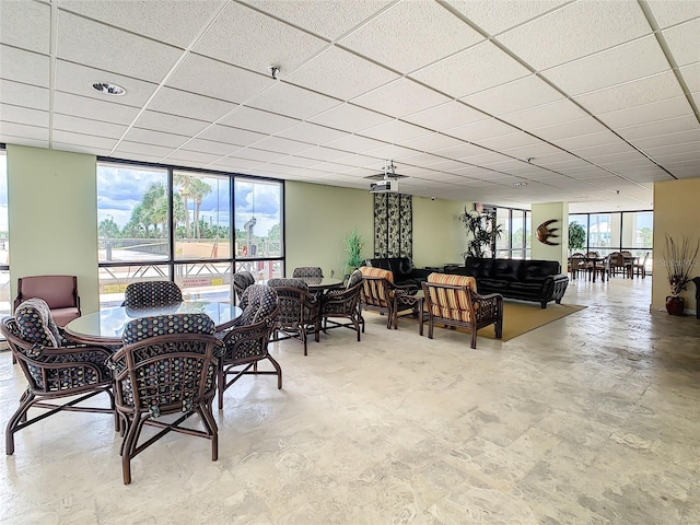 dining area featuring floor to ceiling windows, a drop ceiling, and a healthy amount of sunlight