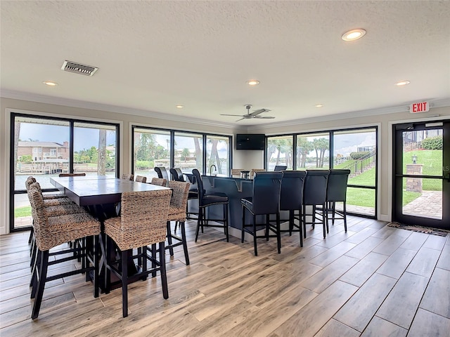 dining room with ceiling fan, light hardwood / wood-style floors, crown molding, and a textured ceiling