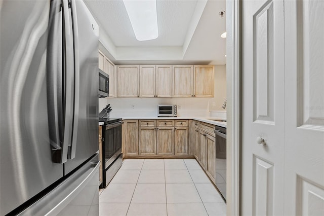 kitchen with appliances with stainless steel finishes, sink, a tray ceiling, light brown cabinets, and light tile patterned flooring